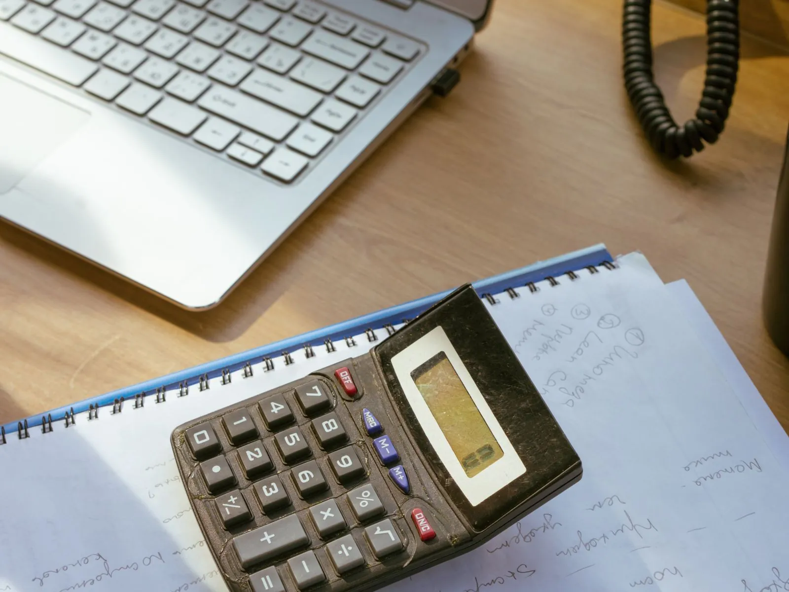 Calculator on ledger sheets and financial reports beside a laptop