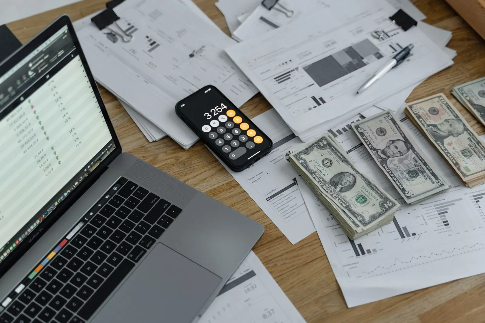 Laptop spreadsheet, calculator and financial reports on a desk, viewed from above
